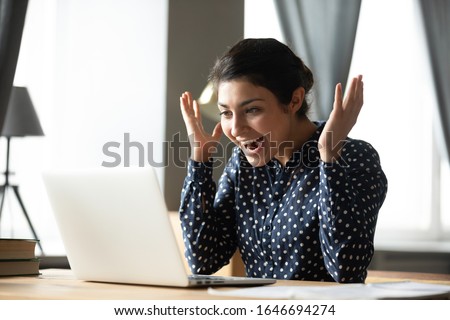 Excited young Indian woman sit at desk using laptop surprised with unexpected online lottery win, overjoyed stunned millennial ethnic girl read receive unbelievable good news on computer Royalty-Free Stock Photo #1646694274