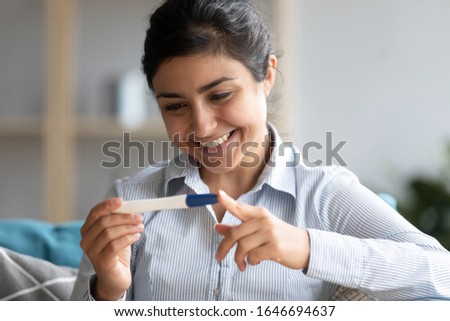 Happy young Indian woman look at positive ovulation pregnancy test results at home, smiling millennial ethnic girl get pregnant see two stripes on stick, future maternity, fertility, ivf concept Royalty-Free Stock Photo #1646694637