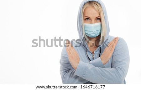 Woman wearing face mask. Woman with flu sneezing, a woman in a hoodie in winter clothing wearing mask to her nose in cold and flu health concept against air pollution background. Sign with hands stop