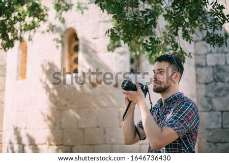A man with a camera near the old temple. Tourist photographer takes pictures of attractions near the ancient stone wall of a castle or temple