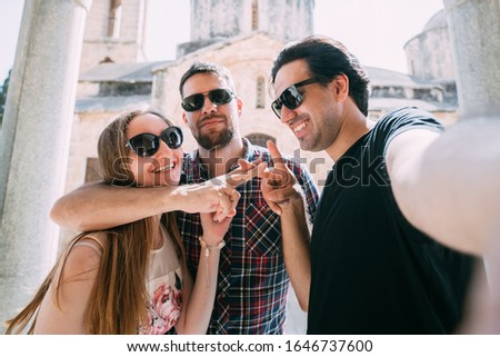 A group of friends takes a selfie against the backdrop of an ancient temple. Two guys and a girl have fun taking pictures near the ancient stone walls of the church
