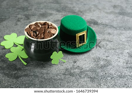 Pot of gold coins, hat and clover leaves on grey stone table. St. Patrick's Day celebration