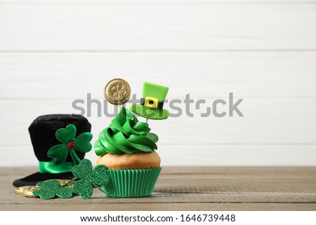 Decorated cupcake and hat on wooden table, space for text. St. Patrick's Day celebration