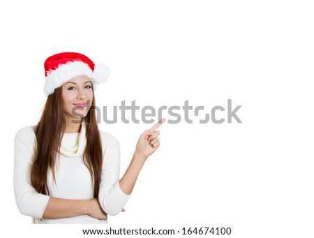 Closeup portrait of beautiful young christmas woman wearing red santa claus hat pointing with index finger to space at right, isolated on white background. Positive human emotions facial expressions