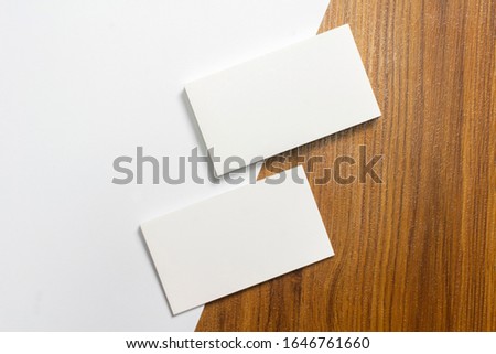 Two blank business cards half of each lie down on white paper and wooden desk background, with 3.5 x 2 inches size as template for design presentation, showcase etc.