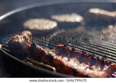 A close up portrait of some delicious barbecue meat on the grill of a bbq. There is a selection of different kinds of meat, like spareribs, chicken drumsticks and hamburgers.