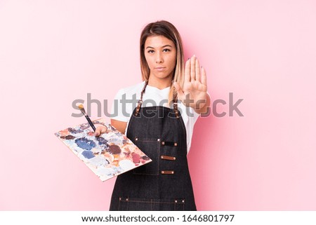 Young artist caucasian woman holding a palett isolated standing with outstretched hand showing stop sign, preventing you.