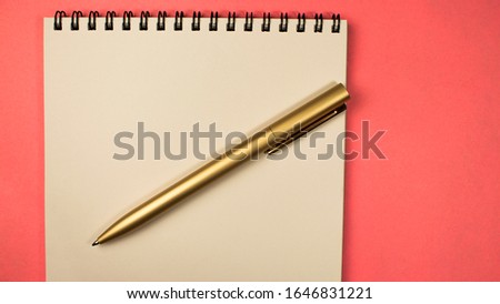 golden pen lies on a notebook on a pink background