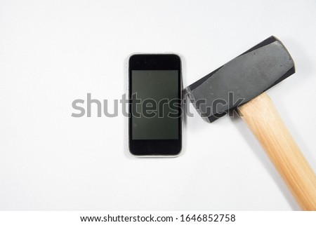 A sledgehammer lays next to a smart phone both in a vertical position. 