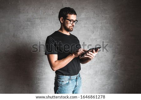 Adult male in trendy glasses and black T-shirt with tablet. on gray background. Business, work, education