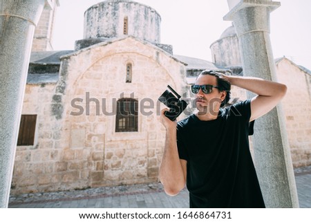Young man with a camera on the background of an ancient temple. Tourist photographer holding a camera near the ancient stone walls of the church