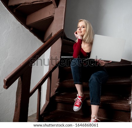 blonde hipster with laptop computer sits on aged stairs in old country house