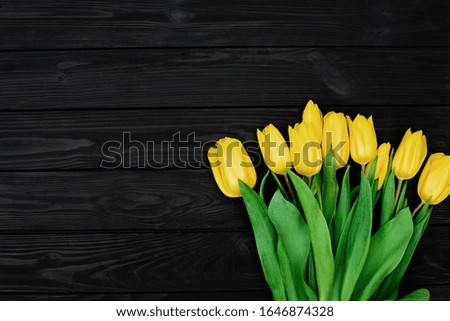 Bouquet of yellow spring tulip flowers on a black wooden background. Flat lay. Copy space. Mothers Day. International Women's Day.