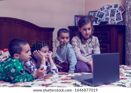 Pretty children looking at computer monitor while laying in bed and eating popcorn. Four young children watching cartoons or movies on a laptop. toned