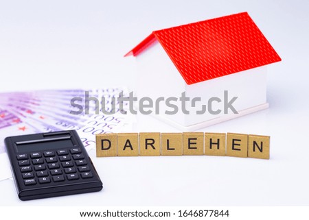 The photo shows a white model house with red roof, letters, banknotes and calculator