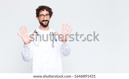 young doctor man smiling and looking friendly, showing number ten or tenth with hand forward, counting down against copy space wall