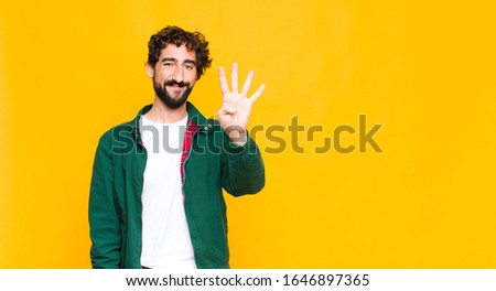 young crazy bearded man smiling and looking friendly, showing number four or fourth with hand forward, counting down against flat wall