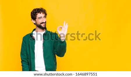 young crazy bearded man feeling happy, relaxed and satisfied, showing approval with okay gesture, smiling against flat wall