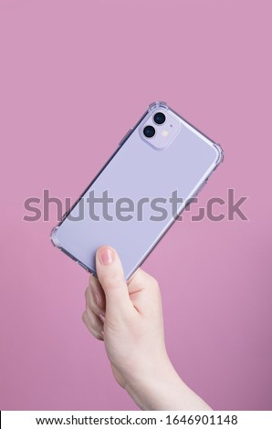 Female hand holding purple iPhone 11 in transparent cover isolated on a pink background. Clear phone case mock up back view Royalty-Free Stock Photo #1646901148