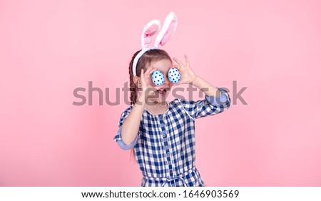 Portrait of a cute little girl with Easter eggs on an isolated pink background. Dressed in a blue plaid dress with a Hoop with Bunny ears. The concept of the Easter holidays.