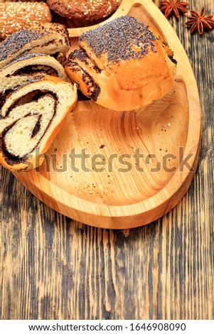 Fresh slices of roll with poppy seeds on a wooden surface, next to cookies, anise stars in blur, close-up, copy space, vertical image.