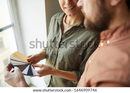 Close up of happy couple looking at color samples standing by window while redecorating house, copy space