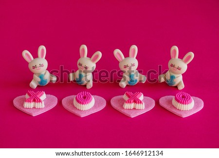 Happy bunnies with eggs and hearts isolated on bright pink background, ready to deliver a loving Easter greeting.