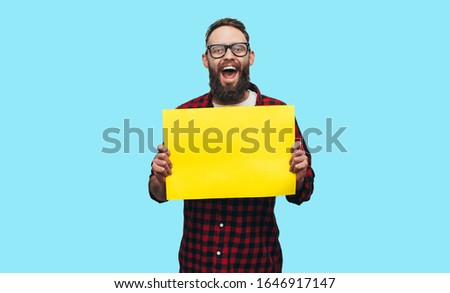 Handsome hipster man holding a blank yellow billboard or poster with blank space for your text isolated on blue background. Discount, sale, season sales.