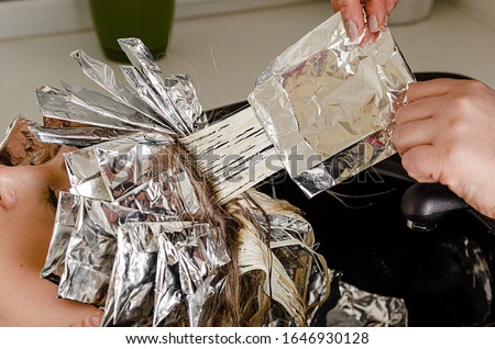 Stylist is taking off the foil from models hair. Bleaching or dyeing process. Beauty salon, fashionable hair coloring with AirTouch technique Royalty-Free Stock Photo #1646930128