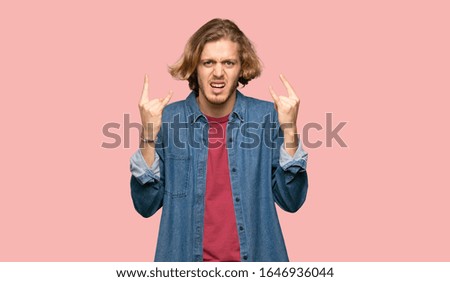 Blonde man making rock gesture on colorful background