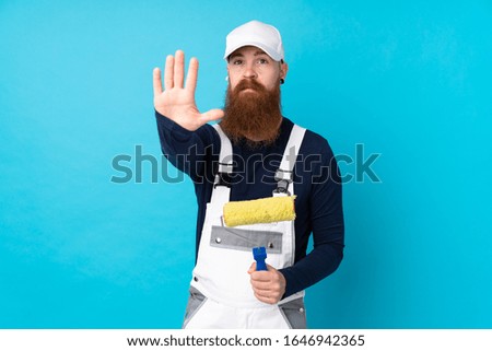 Painter man with long beard over isolated blue background making stop gesture with her hand