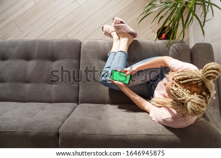 Woman with blond canecalons sitting on sofa and using smartphone with green screen for your image