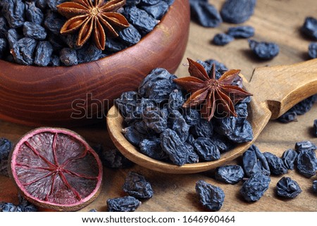 black raisins in a spoon on a wooden table. black raisins and anise stars close up