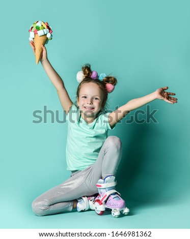 Little kid girl in roller skates sits and hold ice cream in waffles cone with sweets marshmallows candies on white background with free text copy space