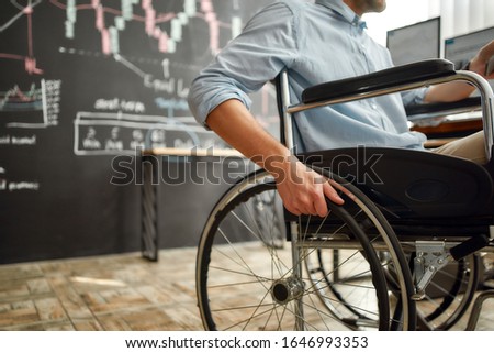 Cropped photo of male office worker in a wheelchair working in the modern office. Disabled man holding a hand on wheel of a wheelchair. Handicapped worker. Trading online. Stock market