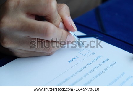 The hand of a woman is signing contract or agreement document arising out of an exchange, consent, commitment about the service or satisfied. It's important to check and ponder before signing, Blurred