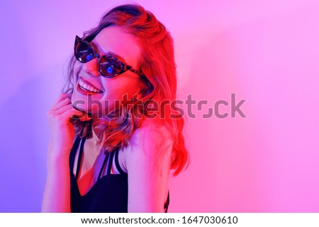Beautiful girl in neon. Fashion photo of a short-haired girl, dancing, sun glasses. Girl in red and blue light posing. Happy girl smiles, laughs, good emotions. Place for text