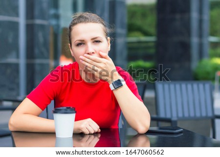 Sleepy, tired, exhausted girl yawns in a cafe with mug, cup of coffee in the morning. Young beautiful woman wants to sleep cover her mouth with hand, looking at camera. overwork and sleep deprivation Royalty-Free Stock Photo #1647060562