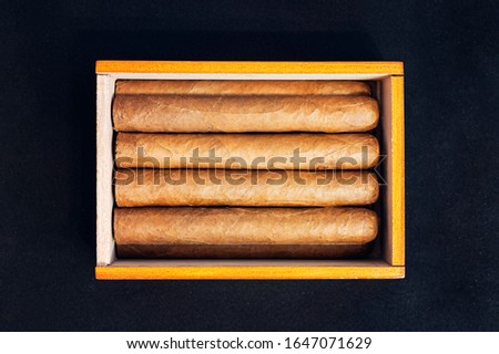 Close up of cigars in open humidor box on black table in the dark.