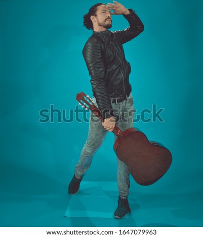 attractive latin man in rock star jacket, on blue background,taking the acoustic guitar like a baseball bat