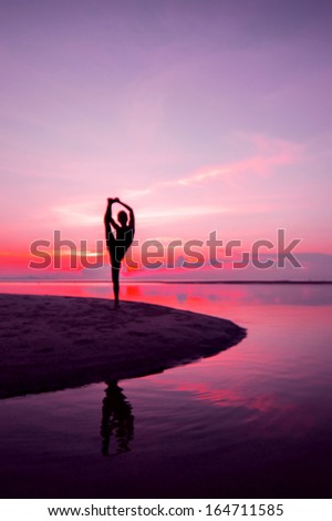 Silhouette woman with yoga posture on the beach at sunset with reflection.