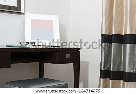 Still life of a bedroom corner with curtains and a writing desk in a luxury hotel room with reading glasses and a pen. Stylish home interior with no people.