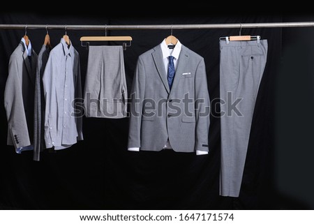 Business mens suits ,pants with long sleeve shirts ,gray sweater hang on hangers -black background


