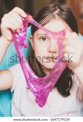 kid looking through hole in pink slime. Preschool girl play with slime. Homemade Slime. Toy for children mucus and liquid flowing on hand. Close up. Slime toy