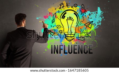 businessman drawing colorful light bulb with INFLUENCE inscription on textured concrete wall, new business idea concept
