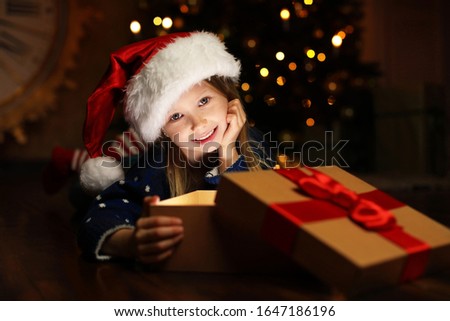 Cute child opening magic gift box near Christmas tree at night