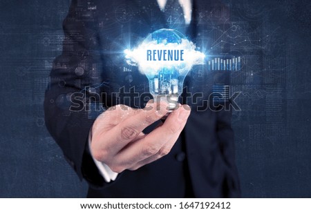 Businessman holding a light bulb with REVENUE inscription, new business concept