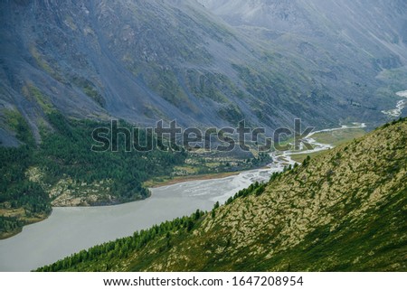 Atmospheric alpine scenery with beautiful valley with mountains lake and giant textured hillside with nature patterns. Awesome aerial view to big rocky hills and huge mountains. Trees on mountainside.