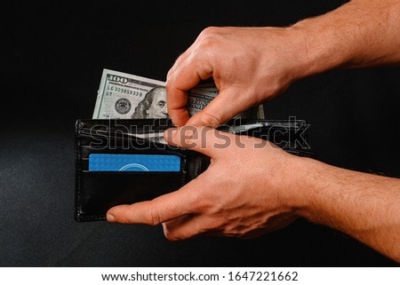 Man on black background holds in his hands a wallet with dollars close up.