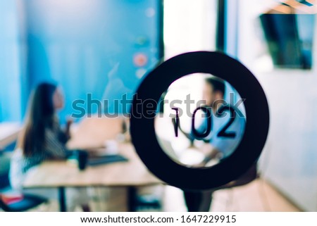 Blurred business people working together and talking while sitting at table in conference room number 102 with glass transparent wall